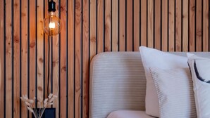 A modern room with a wooden slat wall, a white sofa with a striped throw, and a small side table with a vase and a lamp. - Eggert Alm Apartments (Ilsenburg (Harz))