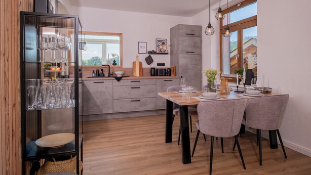A modern kitchen with a dining area, wooden cabinets, and a large window. - Eggert Alm Apartments (Ilsenburg (Harz))