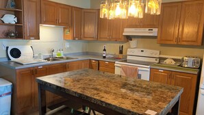 A kitchen with wooden cabinets, a granite countertop, a stove, a sink, and a dining table with stools. - "Hook, Line,& Sinker"- At the edge of Erie; 7 days stay plus 1 chartering free
 (Kingsville)