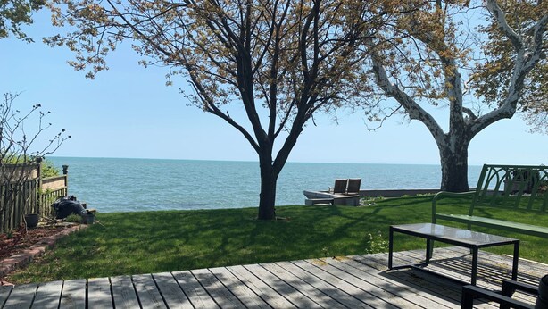 A wooden deck with a table and chairs, a grassy area with a tree, and a view of the sea. - "Hook, Line,& Sinker"- At the edge of Erie; 7 days stay plus 1 chartering free
 (Kingsville)