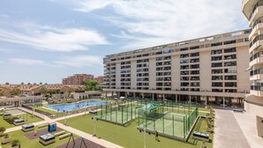 Een hotel met meerdere verdiepingen, een zwembad, tennisbanen en een verzorgd gazon.