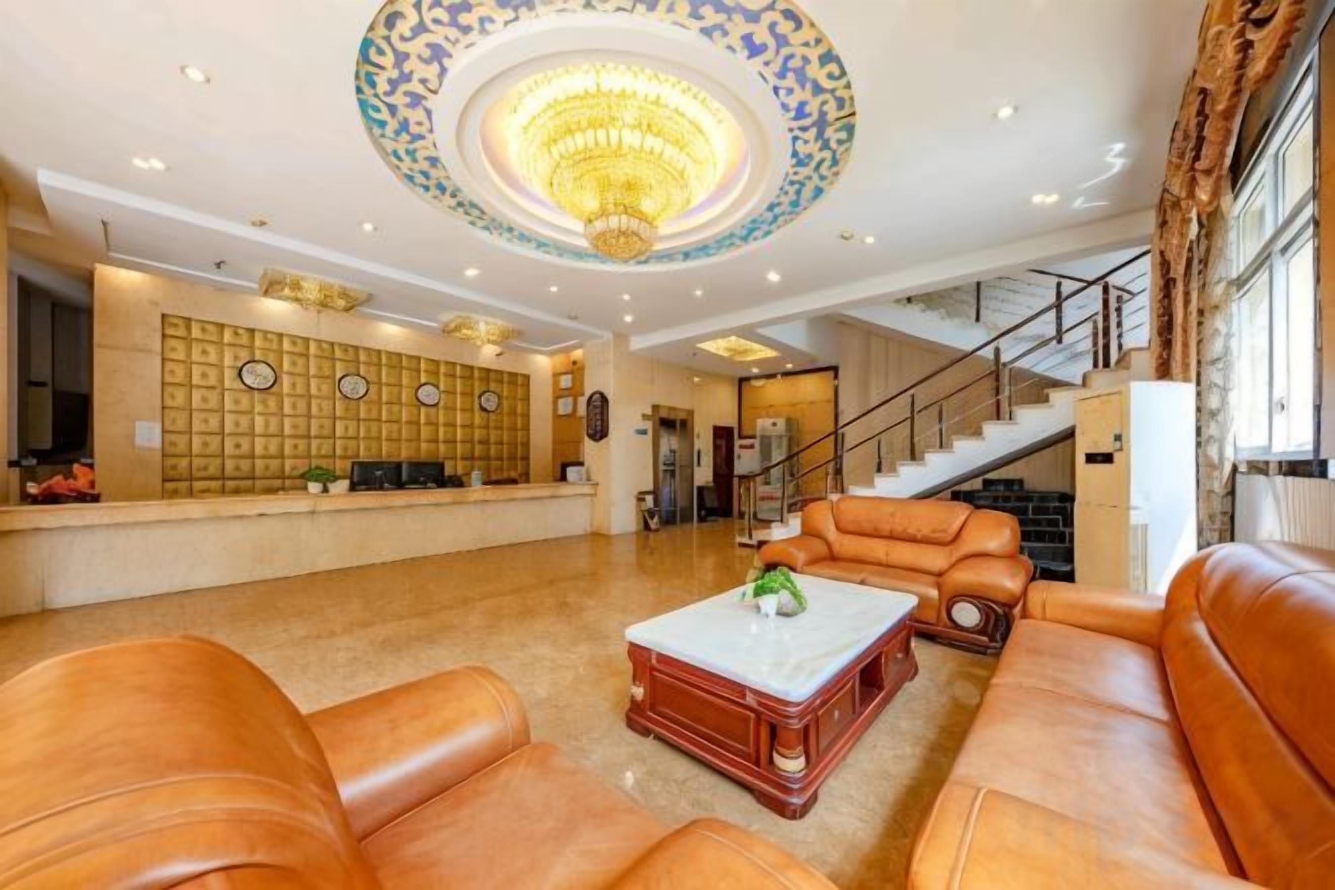 A lobby with leather sofas, a reception desk, a staircase, and a chandelier.