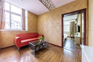 A room with a red sofa, a glass coffee table, wooden flooring, a patterned wall, and a doorway leading to another room.