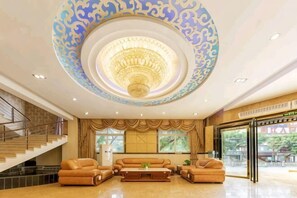 Un vestíbulo espacioso con una imponente lámpara de cristal, sofás de cuero, una escalera y ventanas amplias.