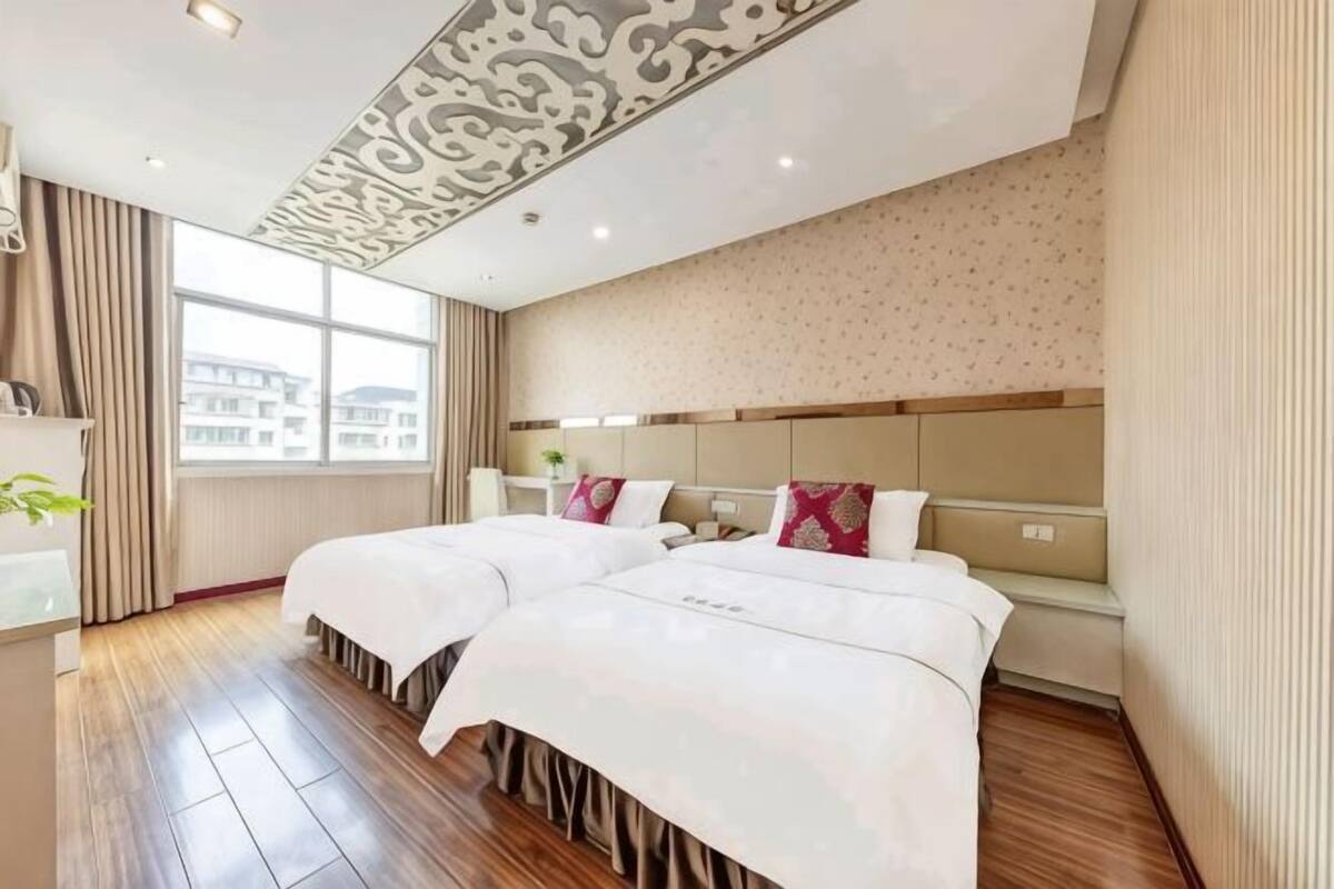 Une chambre d’hôtel avec deux lits, une grande fenêtre et un plafond décoré de motifs.