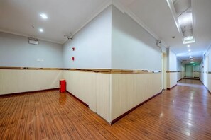 Corredor de hotel com piso de madeira, paredes brancas e uma lixeira vermelha.