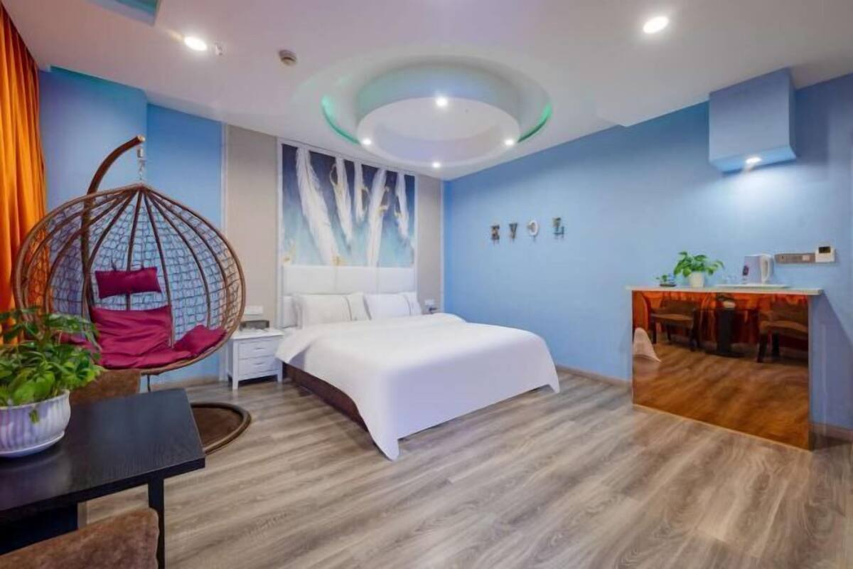 Une chambre moderne avec un fauteuil suspendu, un lit, un bureau et un mur agrémenté d’un luminaire.
