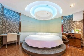 A circular bed with a white bedspread, a desk with a chair, and a small table with a plant. - Huangting Holiday Hotel (Dianjiang County)
