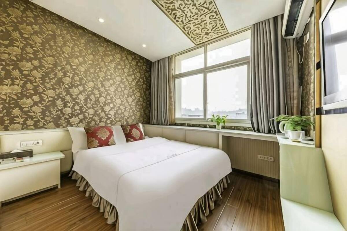 Une chambre d’hôtel avec un grand lit, un canapé, une fenêtre avec des rideaux et une plante posée sur une table d’appoint.