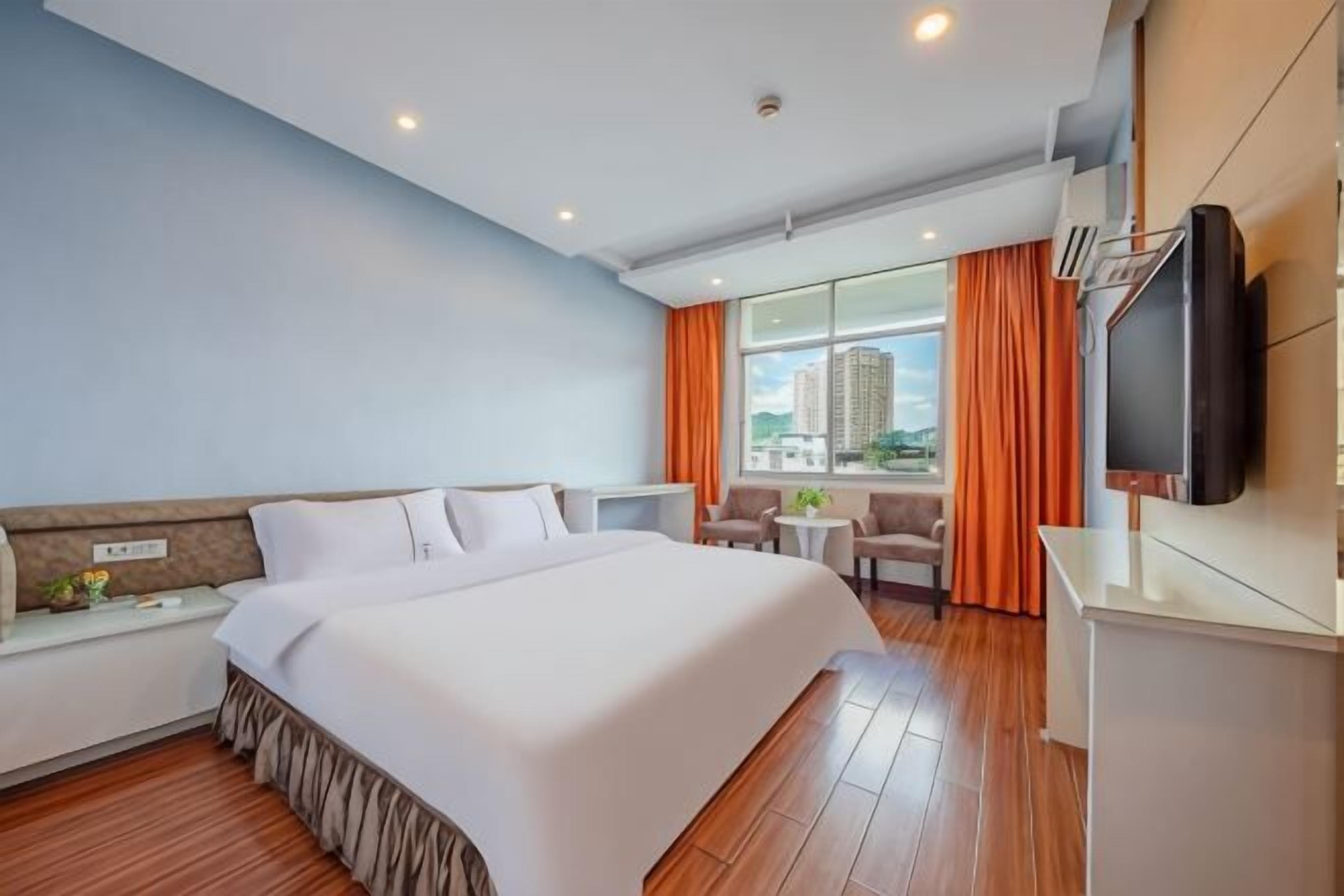 Habitación de hotel con una cama grande, un escritorio, un televisor y vista a la ciudad.