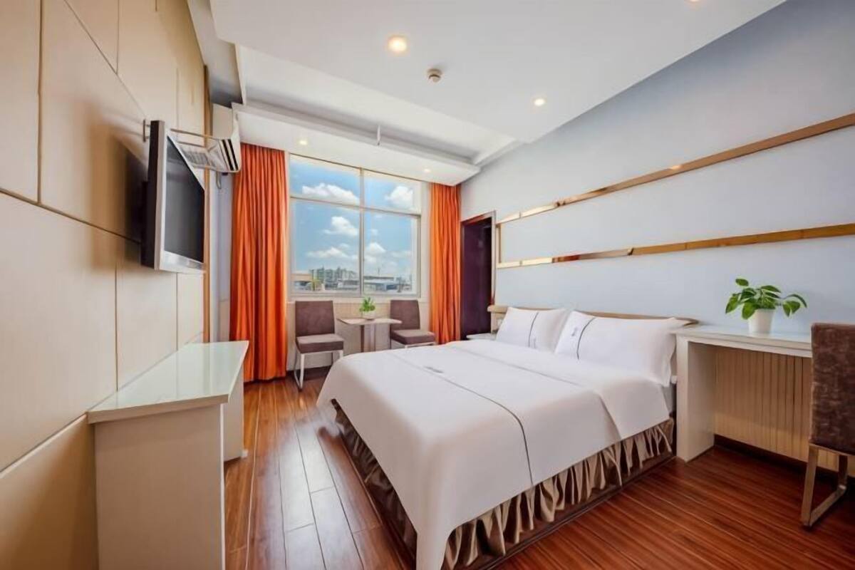 Une chambre d’hôtel avec un lit, un bureau, une chaise, une télévision et une fenêtre avec des rideaux.