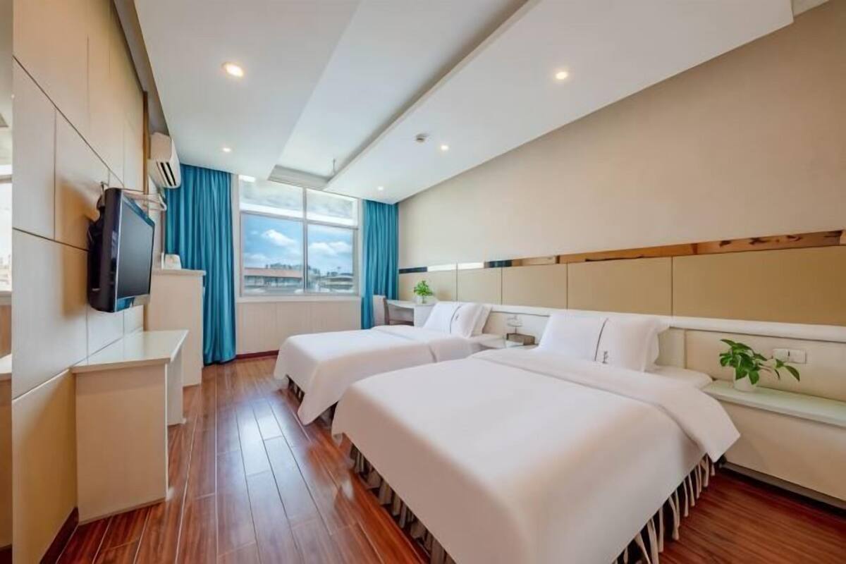 Une chambre d’hôtel avec deux lits, une télévision, un bureau et une fenêtre avec des rideaux.