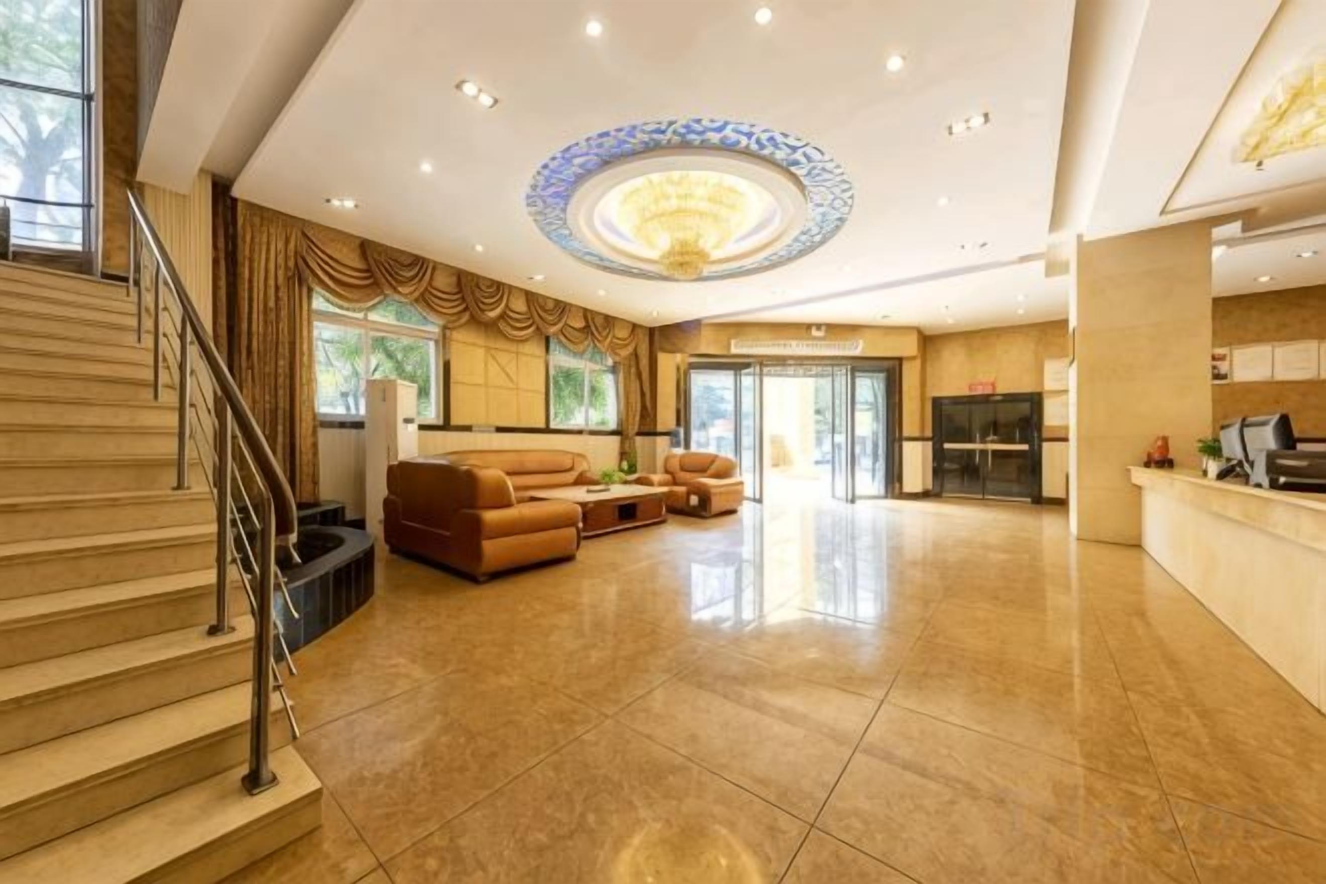 A spacious lobby with a grand staircase, a seating area with leather sofas, and a reception desk.