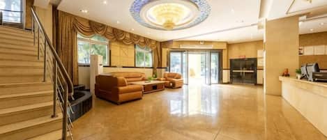 A spacious lobby with a grand staircase, a seating area with leather sofas, and a reception desk.