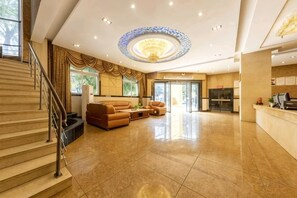 A spacious lobby with a grand staircase, a seating area with leather sofas, and a reception desk. - Huangting Holiday Hotel (Dianjiang County)