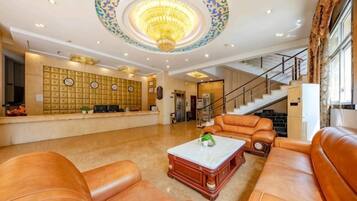 Eine Lobby mit Ledersofas, einem Empfangstresen, einer Kandelaber und einer Treppe.