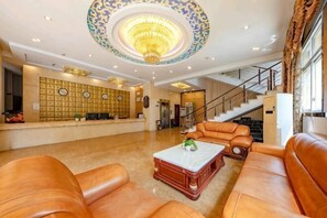 A lobby with leather sofas, a reception desk, a chandelier, and a staircase.