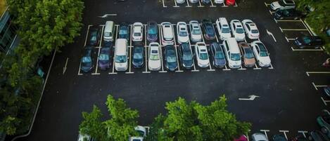 An aerial view of a parking lot with multiple rows of parked cars and trees surrounding the area.
