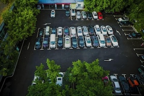 Vista aérea de um estacionamento com várias fileiras de carros estacionados e árvores ao redor.
