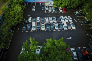 Vista aérea de um estacionamento com várias fileiras de carros estacionados e árvores ao redor.
