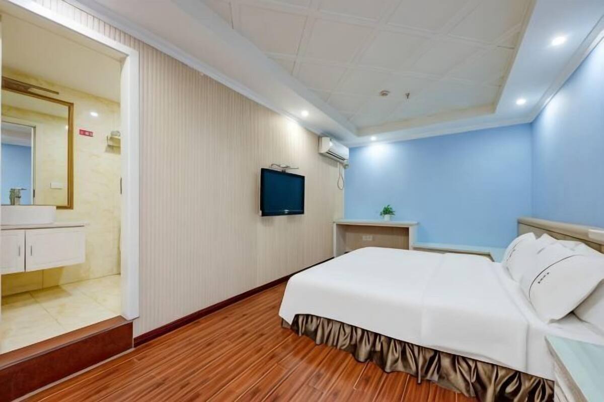 Une chambre d’hôtel comprenant un lit, une télévision, une petite table et une salle de bain avec un miroir et un lavabo.