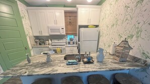 Cozinha com armários brancos, micro-ondas, fogão, geladeira e pia. Há três banquetas no balcão.