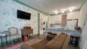 Uma sala de estar com um sofá marrom, uma poltrona estampada e uma TV de tela plana fixada na parede.
