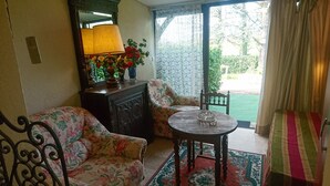 Una stanza con un divano floreale, un tavolo di legno con un vaso di fiori, uno specchio e vista su un giardino attraverso una porta in vetro.