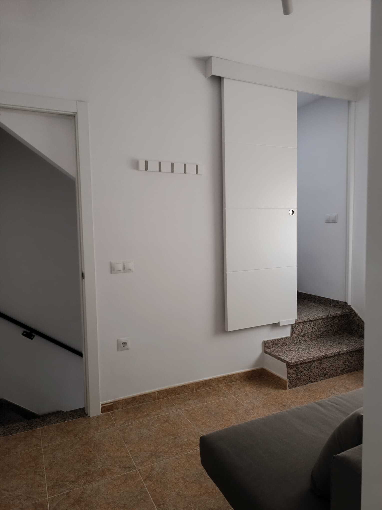 Eine Treppe führt zu einer oberen Etage, eine weiße Wand mit einem Lichtschalter und eine Tür.