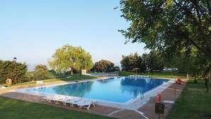 Une piscine rectangulaire entourée d’une terrasse dallée, elle-même bordée d’une pelouse bien entretenue et d’arbres.