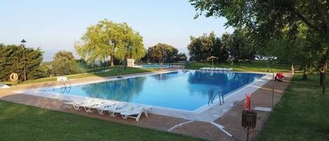A rectangular swimming pool with a paved deck, surrounded by a well-maintained lawn and trees.