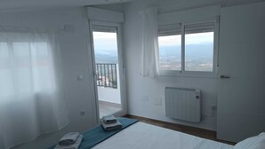 Une chambre à coucher avec un lit, une fenêtre donnant sur un beau paysage, un radiateur et une porte qui mène à un balcon.
