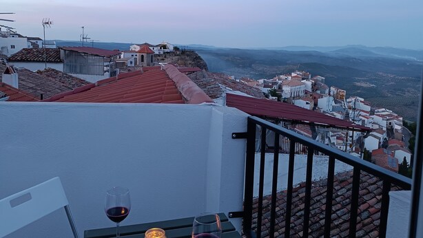 Un balcon avec une table, deux verres de vin rouge et une bougie allumée.