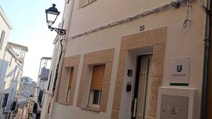 Une rue étroite bordée d’un immeuble doté d’un balcon, de nombreuses fenêtres et d’une porte portant le numéro 39.