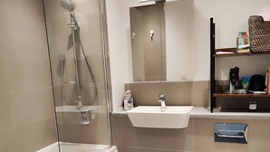A modern bathroom with a glass-enclosed shower, a white sink, and a toilet. -  Spare Bedroom,  Wembley Stadium
 (London)