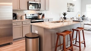 A modern kitchen with a central island, stainless steel appliances, wooden bar stools, and pendant lighting. - Lakefront, Dock, Kayaks, Paddleboards, Pool,Hot tub and access to boat rentals! (Eatonton)
