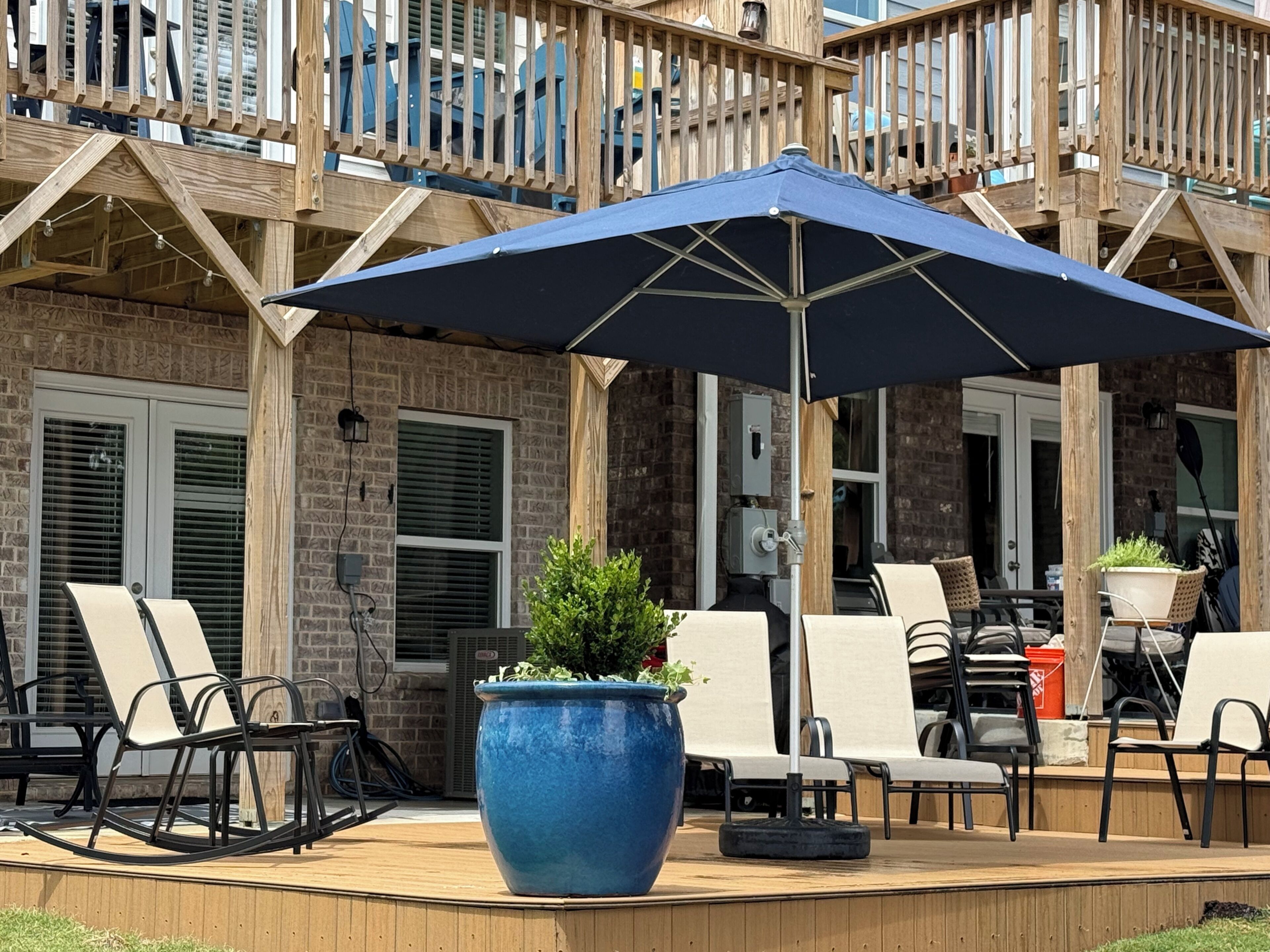 A deck with outdoor seating, a large blue umbrella, and a potted plant.