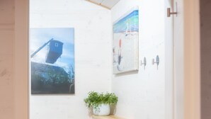 Une petite salle de bain avec des toilettes blanches, un plancher en bois, une petite étagère avec une plante et deux tableaux encadrés au mur.