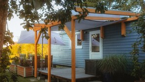 Une pergola en bois avec un patio couvert, une terrasse en bois et une porte donnant accès à une maison aux bardages bleus.
