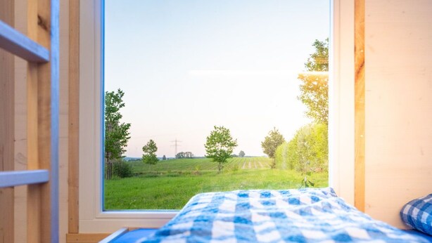 Une chambre avec une grande fenêtre, une couvre-lit à carreaux et des murs en bois.