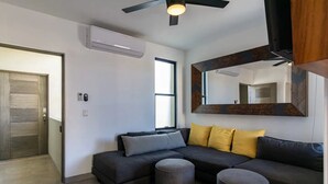 Una sala moderna con un sofá modular, dos otomanas, un ventilador de techo y un espejo grande.