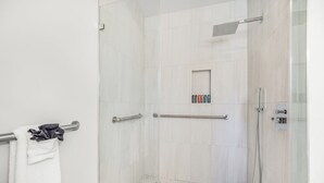 Eine moderne Dusche mit Glastür, einem Handtuchhalter mit weißem Handtuch und einer kleinen Ablage für Toilettenartikel.