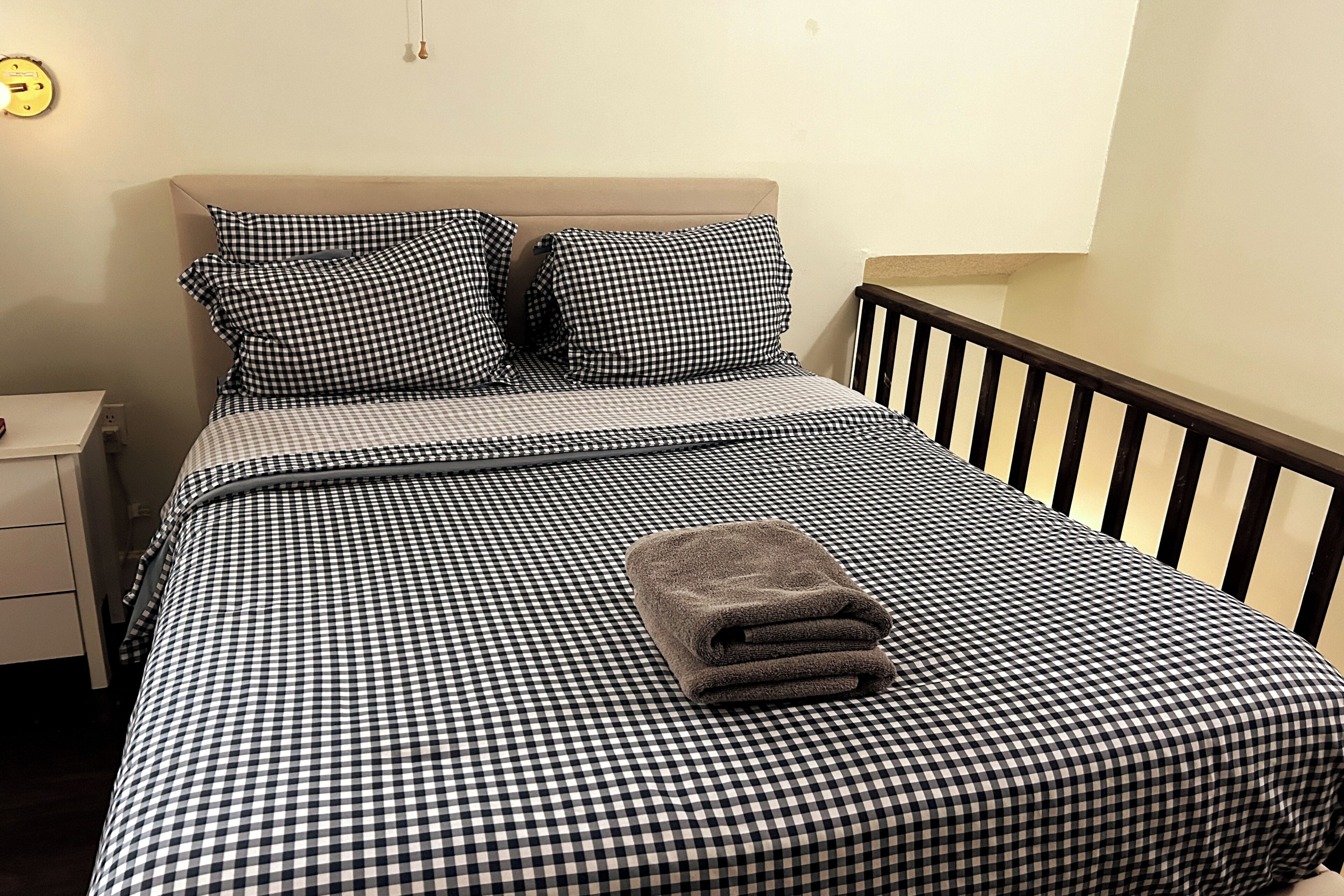 A bed with a checkered bedspread, two pillows, and a folded towel.