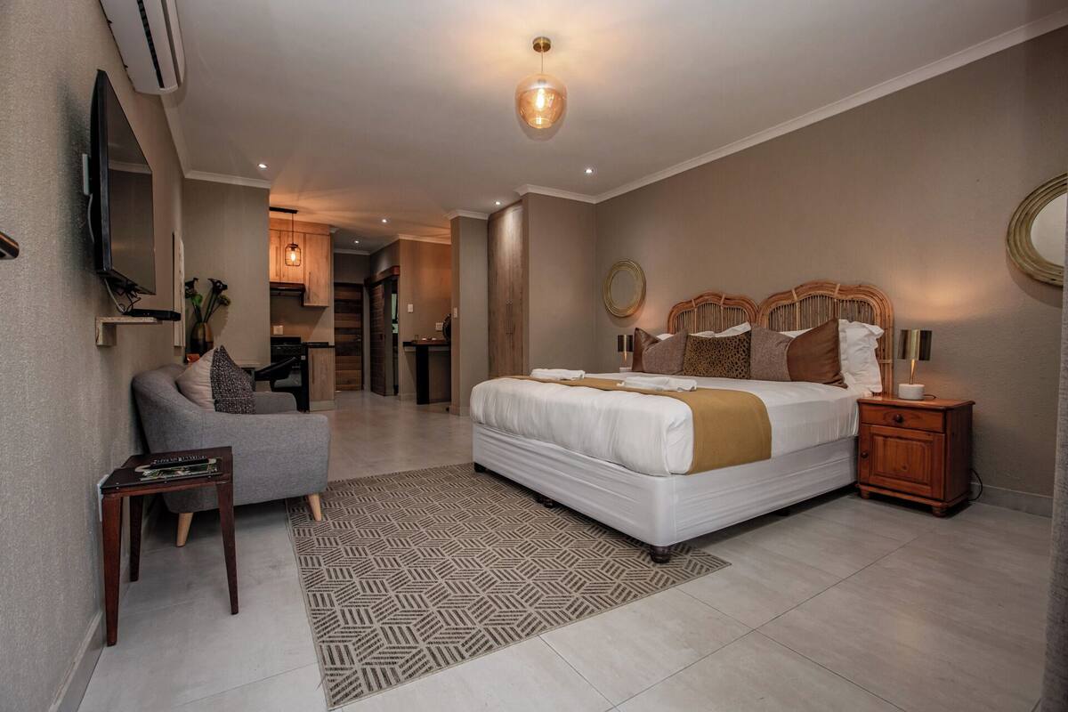 Habitación de hotel moderna con una cama grande, televisión montada en la pared, una zona de estar pequeña y una kitchenette.