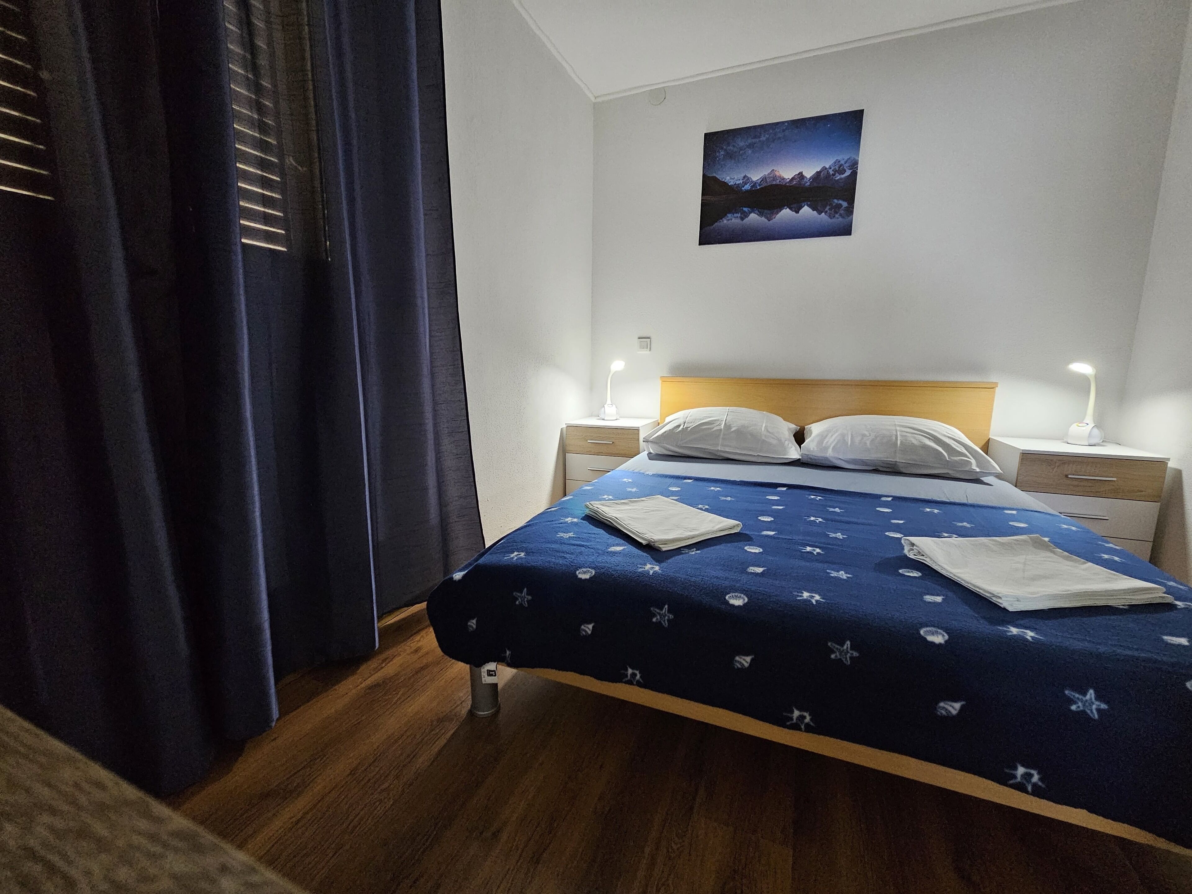 Un lit bien fait, recouvert d’une couvre-lit bleue, avec deux oreillers blancs et une table de chevet sur laquelle se trouve une lampe.