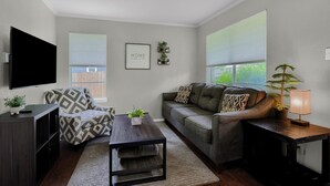 Un salon comprenant un canapé, un fauteuil, une table basse, un téléviseur et une petite plante.
