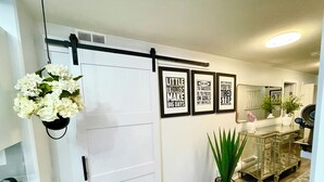 A hallway with a white door, a black-framed mirror, a potted plant, and motivational posters on the wall. - Luxury Suite-Unique Quotes Space (Saskatoon)