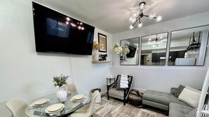 A modern living room with a dining area, a grey sofa, a patterned armchair, and a large flat-screen TV mounted on the wall. - Luxury Suite-Unique Quotes Space (Saskatoon)