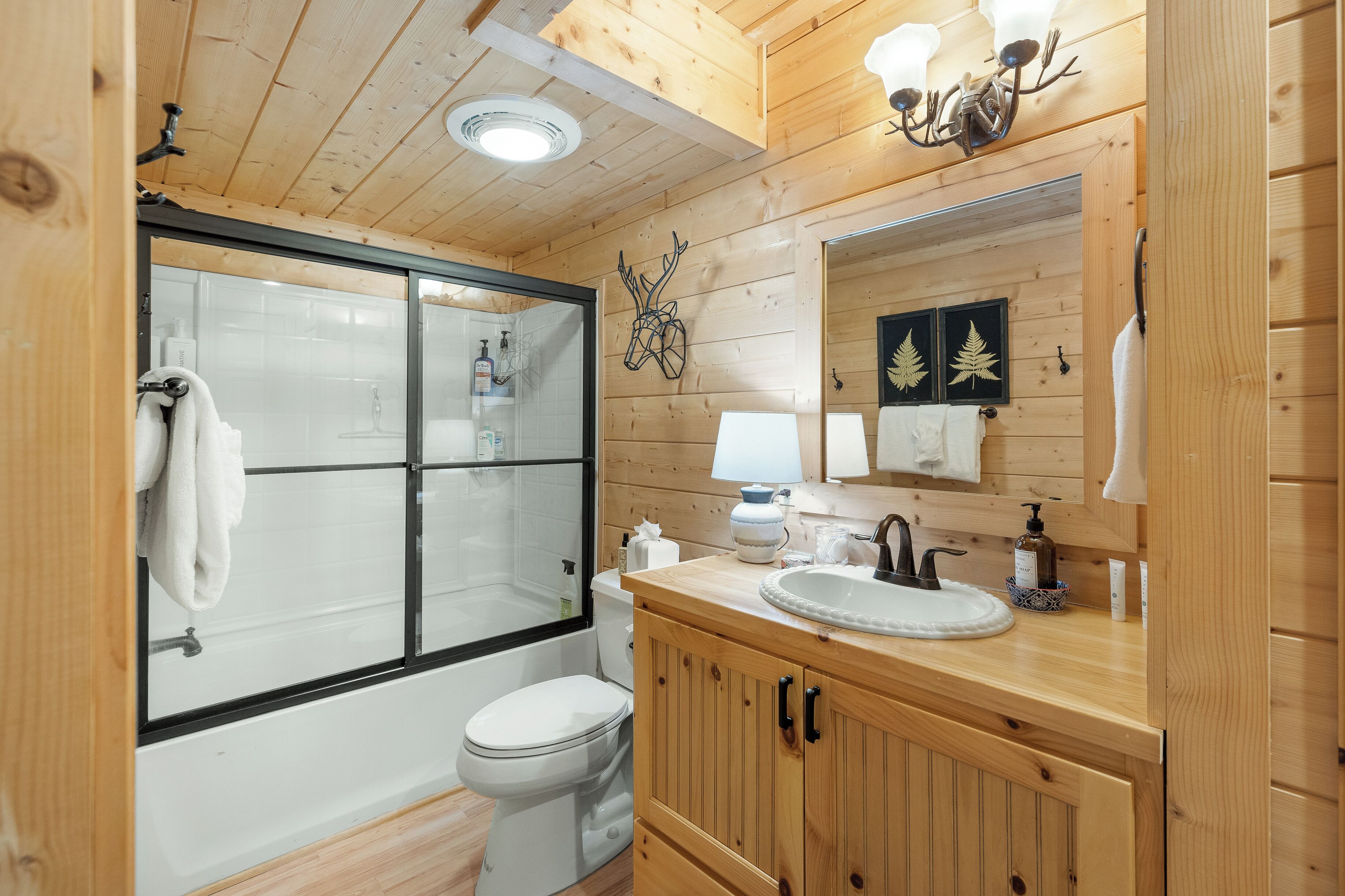 Une salle de bain rustique, avec une cabine de douche en verre, des toilettes blanches, un meuble-lavabo en bois et un miroir.