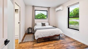 A bedroom with a bed, a window, an air conditioning unit, and a wooden floor. - Pet-Friendly Modern 2BR Duplex in Polson – Walk to Flathead Lake & EV Charging (Polson)
